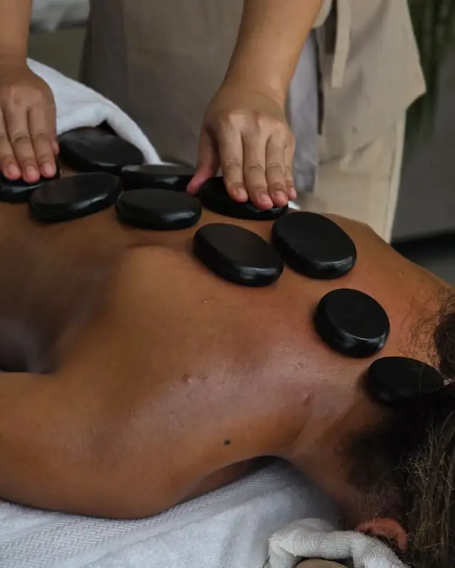 Therapist placing warm stones on the back during a hot stone massage at home in Dubai