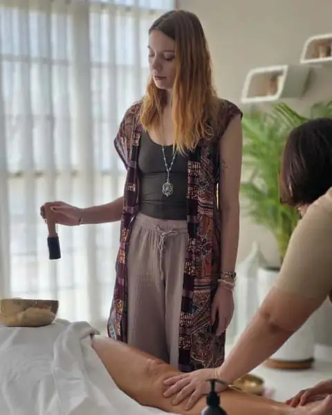 Sound healer playing a chime while a therapist massages the legs during a sound healing massage in Dubai
