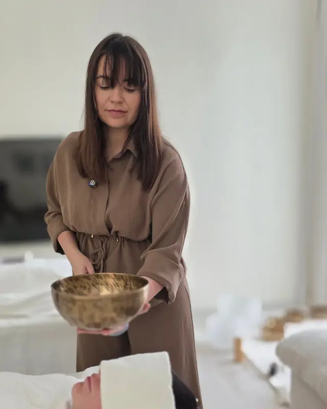 Sound healer holding a singing bowl over a client during a sound healing massage at home in Dubai
